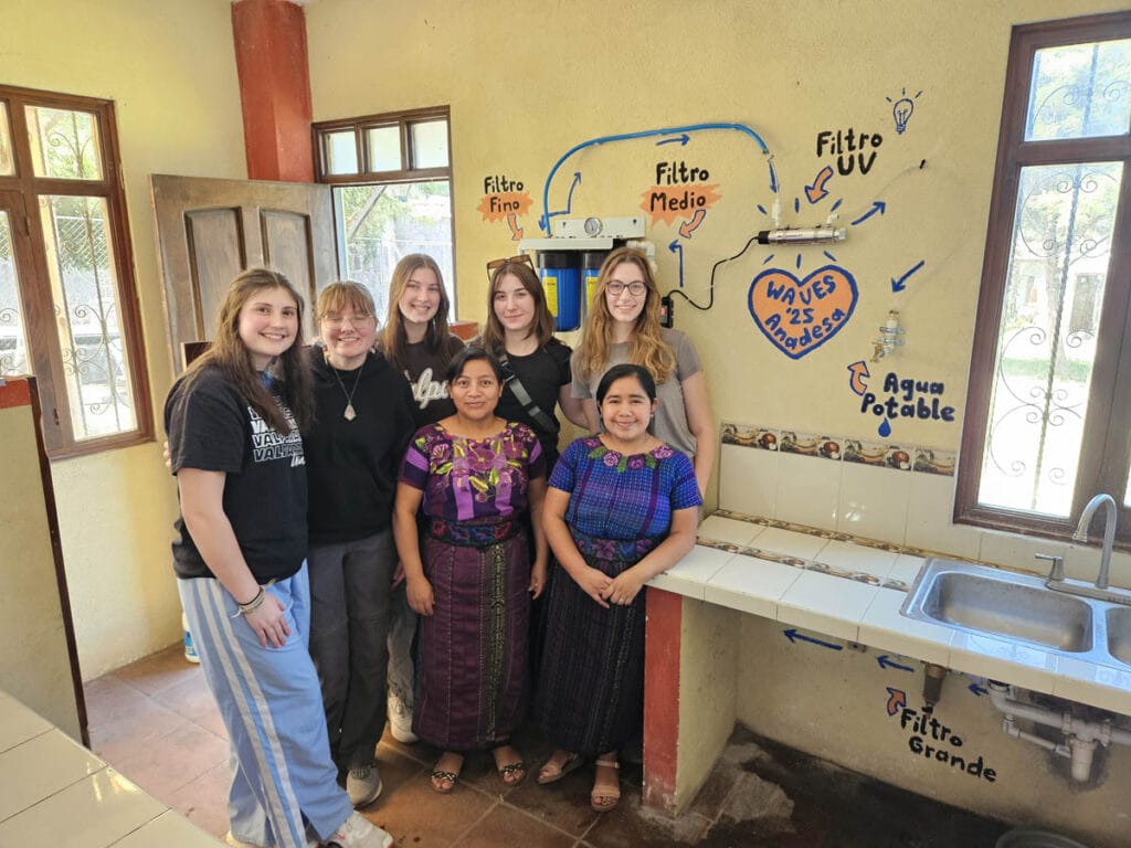 A group of six women posing for a picture in a room with a a water purification project in Guatemala.