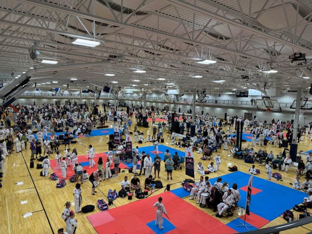 A large group of people are gathered in a gym, practicing martial arts.